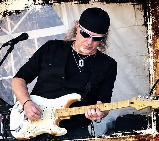 John McAfee playing a white electric guitar